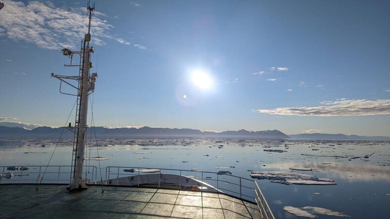 Ship deck in sunlight on open water, surrounded by floating ice sheets