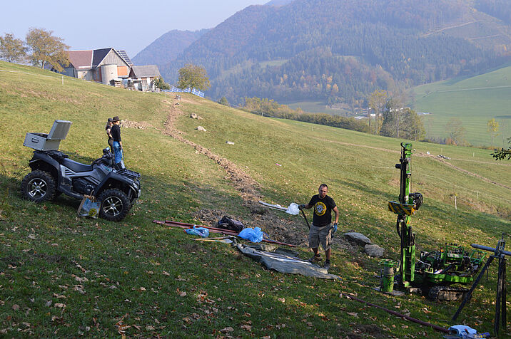 Researchers in the field, setting up their technical equipment, mountains and houses in the background
