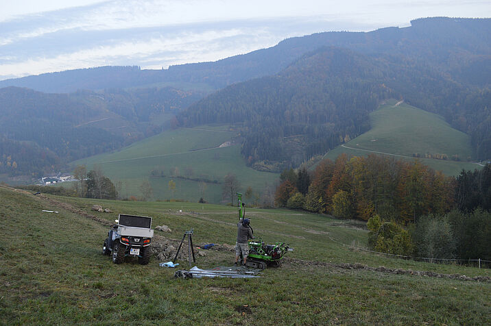 Researcher setting up technical equipment on a hill, mountains and woodlands in the background