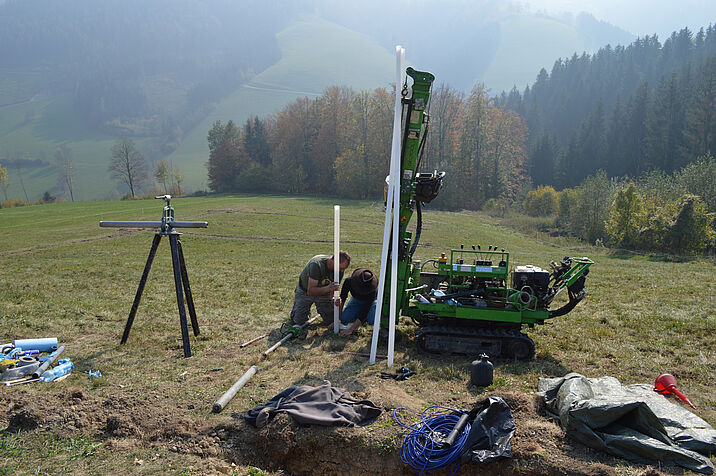 Researchers in the field, setting up their technical equipment, a mountain valley and trees in the background