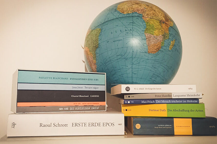 Stack of books (selected works related to the 'Anthropocene Poetics' project), arranged in front of a globe