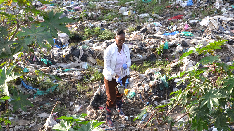 Scientist sampling water at the Nairobi river, large amounts of plastic litter covering the river bank