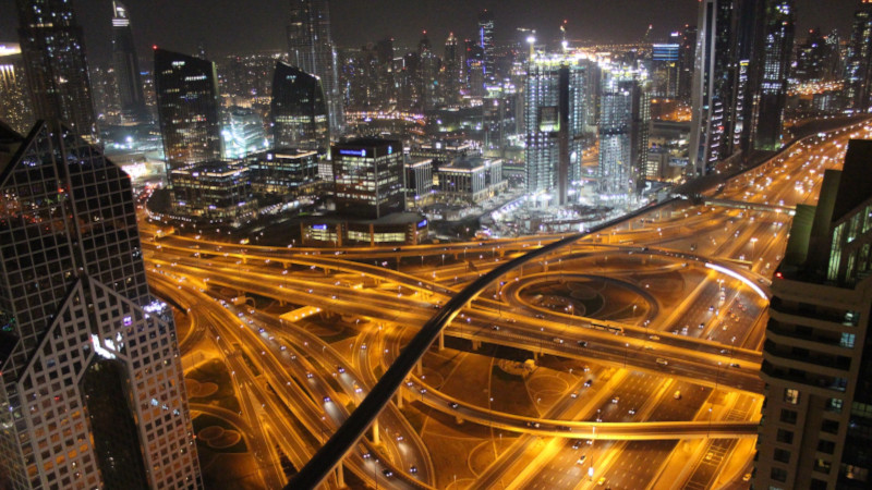 City at night, highway interchange in the foreground, the horizon lined with skyscrapers, millions of artificial light sources in white and orange