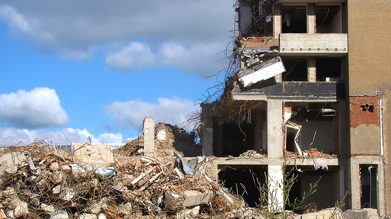Demolished building surrounded by debris, blue sky in the back