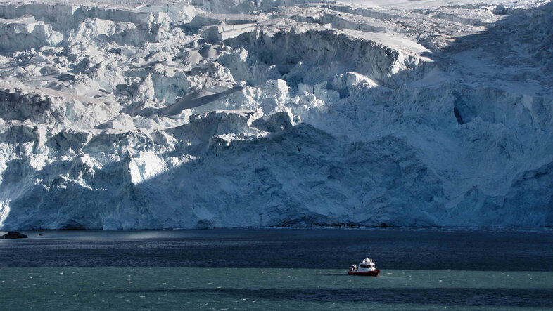 Small boat on the northern sea with a massive ice sheet in the background