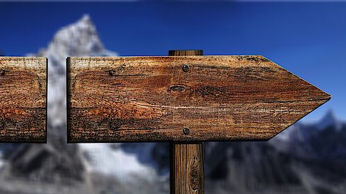Wooden signpost pointing towards the right, a snow-capped mountain in the background