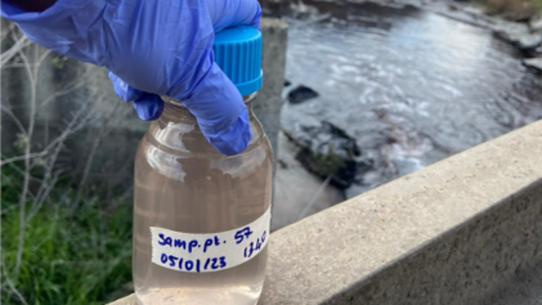 Water sample in a bottle next to a river